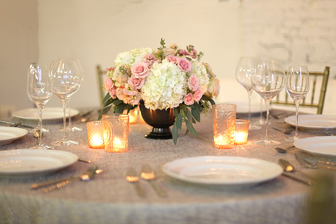 Low centerpiece in a metal compote with blush spray roses, apricot stock, Quicksand roses, white hydrangea and seeded eucalyptus, by Cincinnati wedding florist Floral Verde LLC. 
