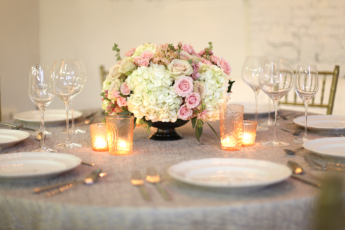Low centerpiece in a large metal compote with blush spray roses, apricot stock, Quicksand roses, white hydrangea and seeded eucalyptus, by Cincinnati wedding florist Floral Verde LLC.
