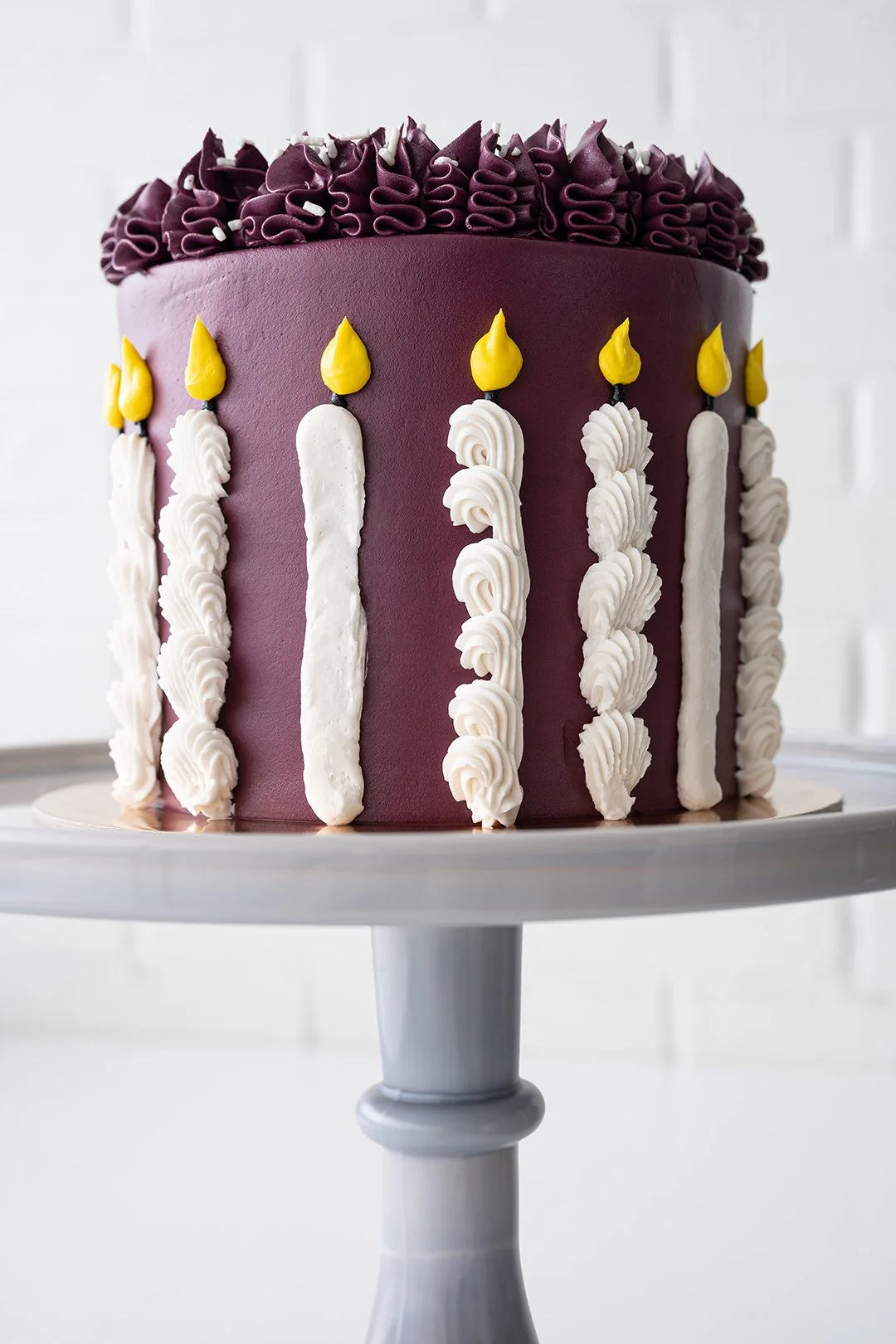 Burgundy Candle Cake decorated with piped buttercream candles, colorful flames, white sprinkles, and ruffled icing.