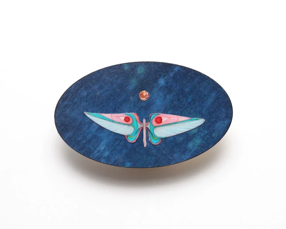 An oval artwork with a blue textured background by Kate Morgan Art features a stylized moth in pastel blue, pink, and teal at the center, with a small golden moon above its head.