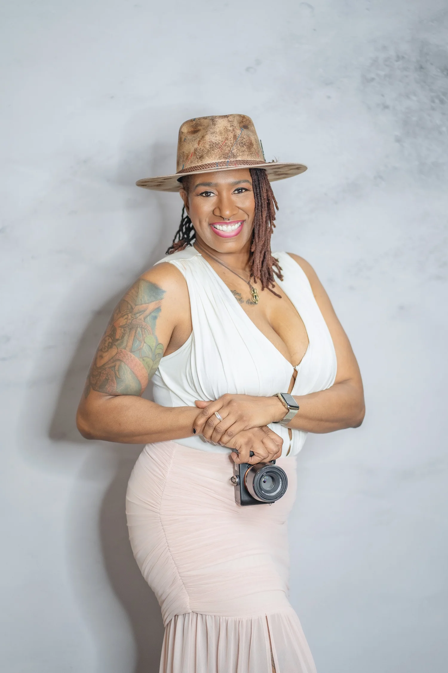 Annette Matthews smiling with her camera, wearing a hat