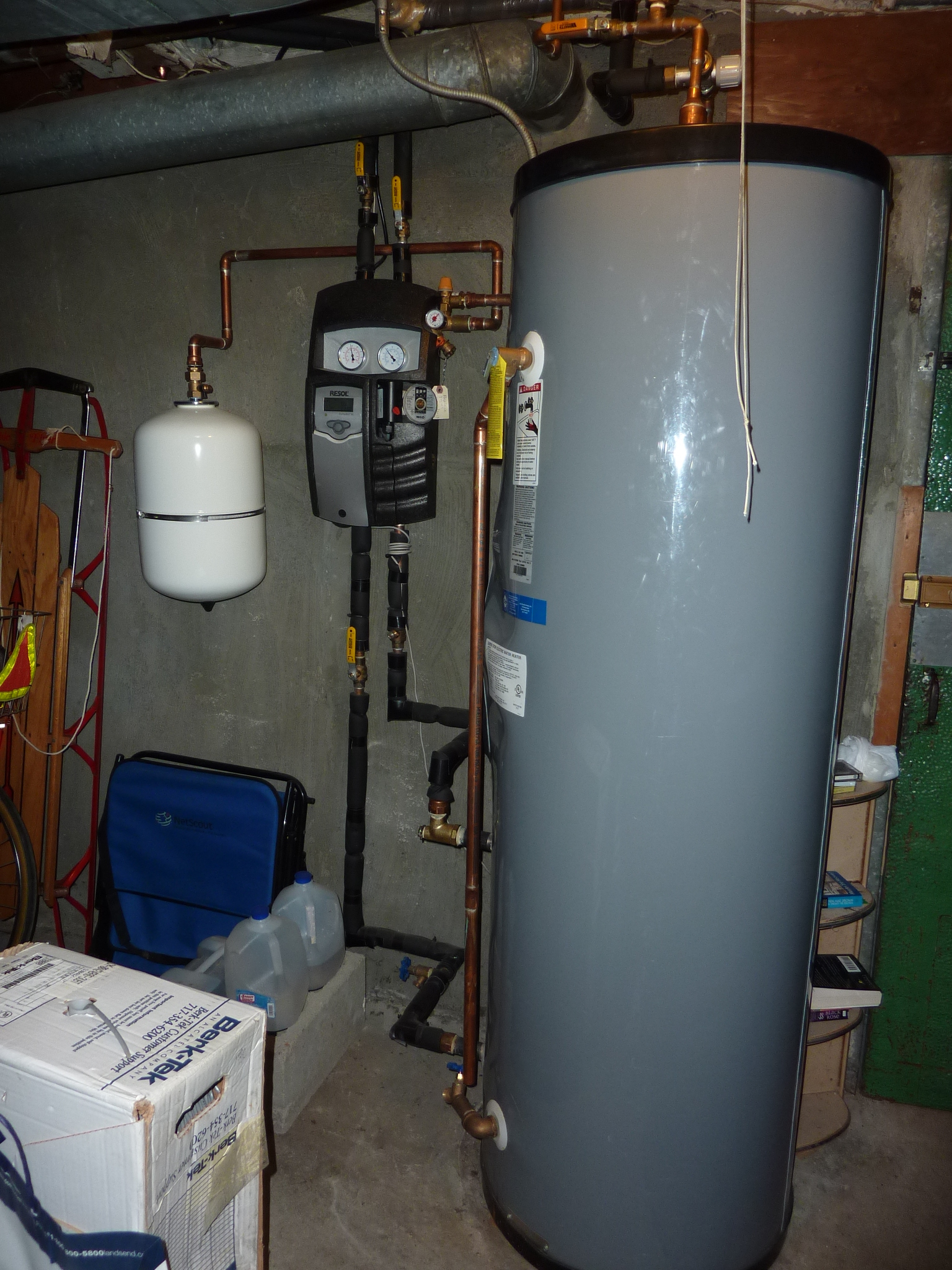 In the basement is a small, white tank for glycol, a pump (center), and an 80-gallon hot water storage tank.