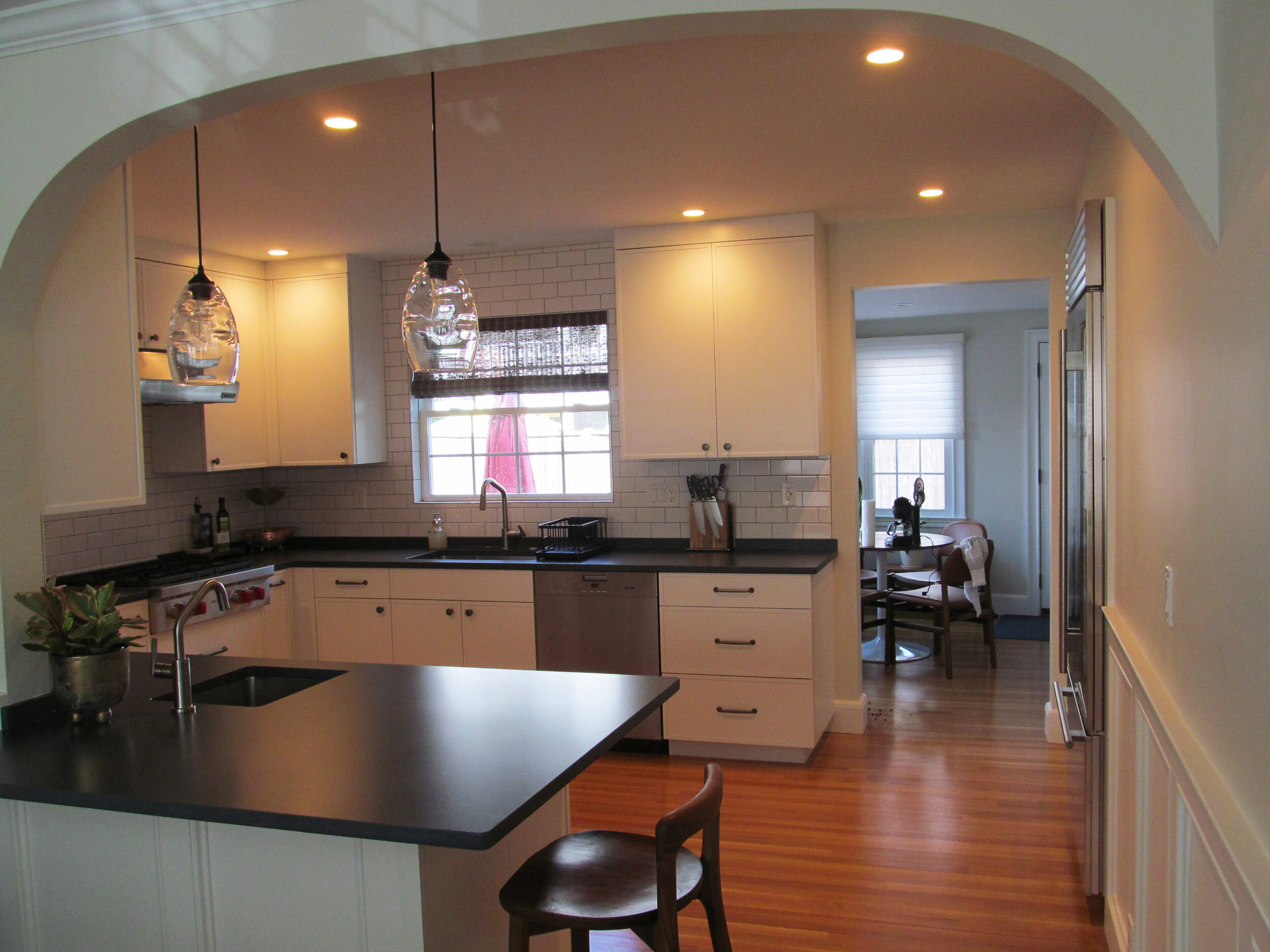 An archway over a peninsula leads into this Brookline kitchen featuring Imperia cabinets painted in Designer White.