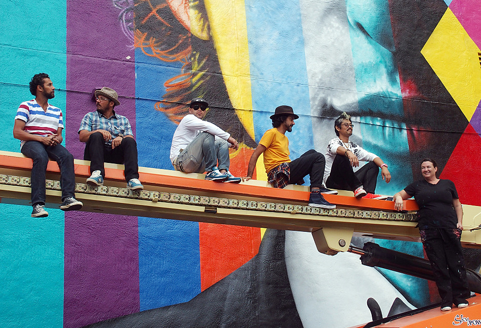 With the mural finished, the crew posed atop the arm of one of the three hydraulic lifts used during the painting. From left to right they are: Agnaldo Brito Pereira, Marcos Rafael da Silva, Silvio Cesar Goncalves de Almeida, Eduardo Kobra, Yuya Nigishi, and Erin Sayer. Nigishi and Sayer are both based in Minneapolis.