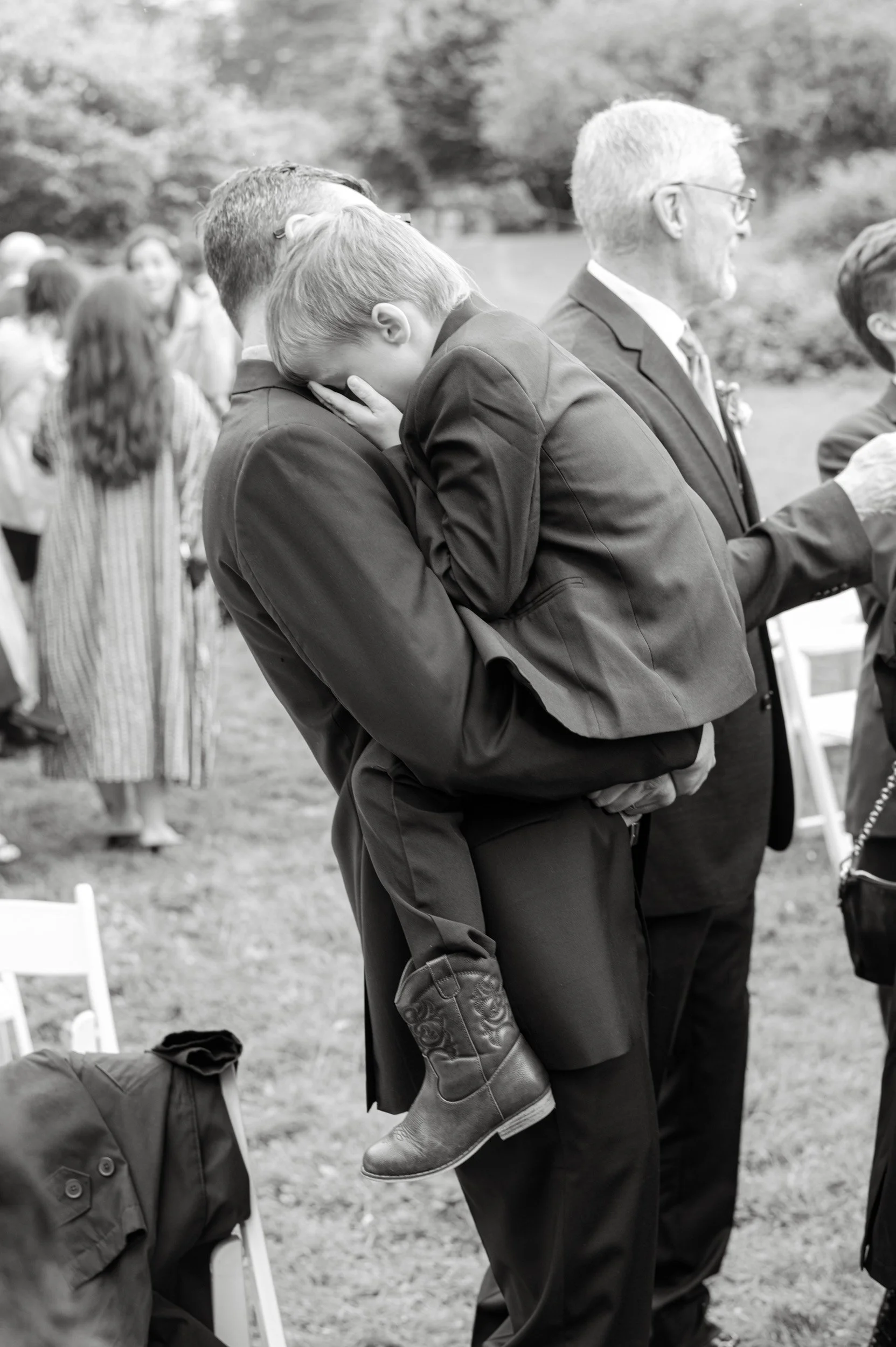 Young stylish child rocks cowboy boots while being held at a wedding.