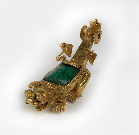 Jaguar pendant. Coclé culture, Sitio Conte, Coclé Province, Panama, AD 700–900. Large pillow-shaped emerald surrounded by four-part gold edging. Outer ones continuous, inner ones bead-like. Pair of decorative, sinuous, "wings" at back of emerald with loose, thin, moveable gold leaf attached. Four legs and feet projecting foreward, each with five similar curving claws, plus one beneath upcurving. Head with rude open mouth full of teeth above and below. Two flat tongues from mouth curving back and ending in scroll at neck. Very bulging eyes at top, almost spherical. Blunt nose with nostrils to sides consisting of four vertical fine-wire sections. Pair of short pointed horns (ears?) on top of head. Long raised tail of rectangular section ending in pair of fixed spiked "wheels." Between them a third wire with loose thin leaf ornament. Small attached horizontal tube between front legs for suspension on chest. This object was excavated in 1940 by J. Alden Mason, curator of the Penn Museum, after golden grave objects were exposed on the banks of the Río Grande de Coclé. Click image to enlarge (Photo courtesy Penn Museum)