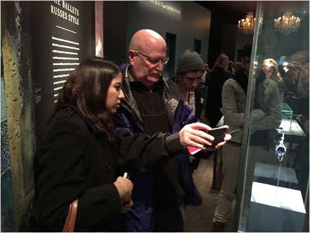 Something(s) missing. Other displays in the Ballets Russes suite were not as successful, such as Marie of Romania's 478-carat blue sapphire, which is the size of a small egg. Richard Hughes, above, noticed that a piece of the sapphire's pavilion appears absent; it was cut for size, not splendor. Below, Billie Hughes's chin can be seen through the gap that a superior stone would not have had. Perhaps with this in mind, the exhibition designers positioned this piece against a busy photomural of garish Ballets Russes dancers. This display reminded the Hugheses—whose Lotus Gemology laboratory specializes in ruby and sapphire—that "Brilliant," aside from its many examples of lovely jewels, does not have a lot to offer cravers of corundum. (Photos: David Hughes)