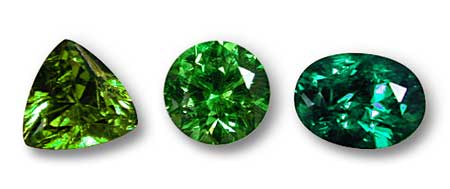 Three green gems, showing a variation in hue position. The round center stone is a straight green, while the trillion-cut stone at left is a more yellowish green and the oval stone at right a slightly bluish green. Generally speaking, hue position is of less importance than saturation. Photo: Wimon Manorotkul
