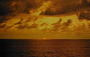 Figure 4. A sunset on the coast of Sri Lanka at Colombo, November, 1988. One can clearly see the strong yellow-orange presence in the direct sunlight. This results from greater scattering of blue-violet wavelengths as the path length of sunlight through the earth’s atmosphere increases towards sundown. It is evident that the use of direct sunlight (as opposed to skylight) just after sunrise or before sundown could definitely enhance the appearance of yellow, orange and red stones. Photo: Richard W. Hughes .