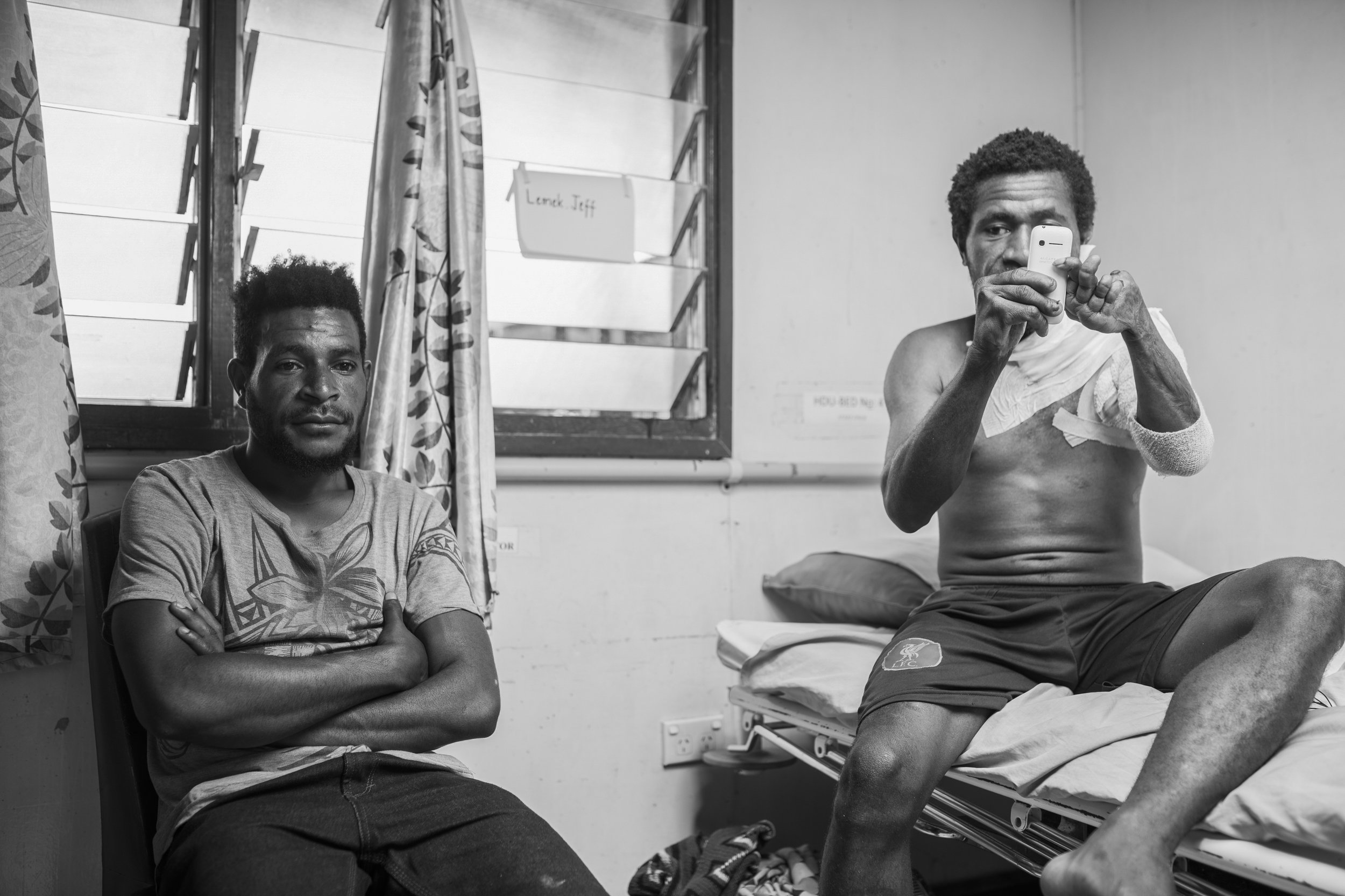Vanimo, Papua New Guinea. Lemeck raises his arms for the first time in his life, and in a surreal moments asks to take my photograph as I've spent three days taking his. To my left, is his younger brother and carer who in the moment looks serious but I knew it came from fatigue after waiting for Lemeck to come our of surgery. We all had a good laugh after this moment, part of exhaustion, but also how Lemeck was suddenly the most mobile he had ever been. He later tore his stitches from moving too much, as it was hard for him to contain his excitment at regaing the use of his left arm.