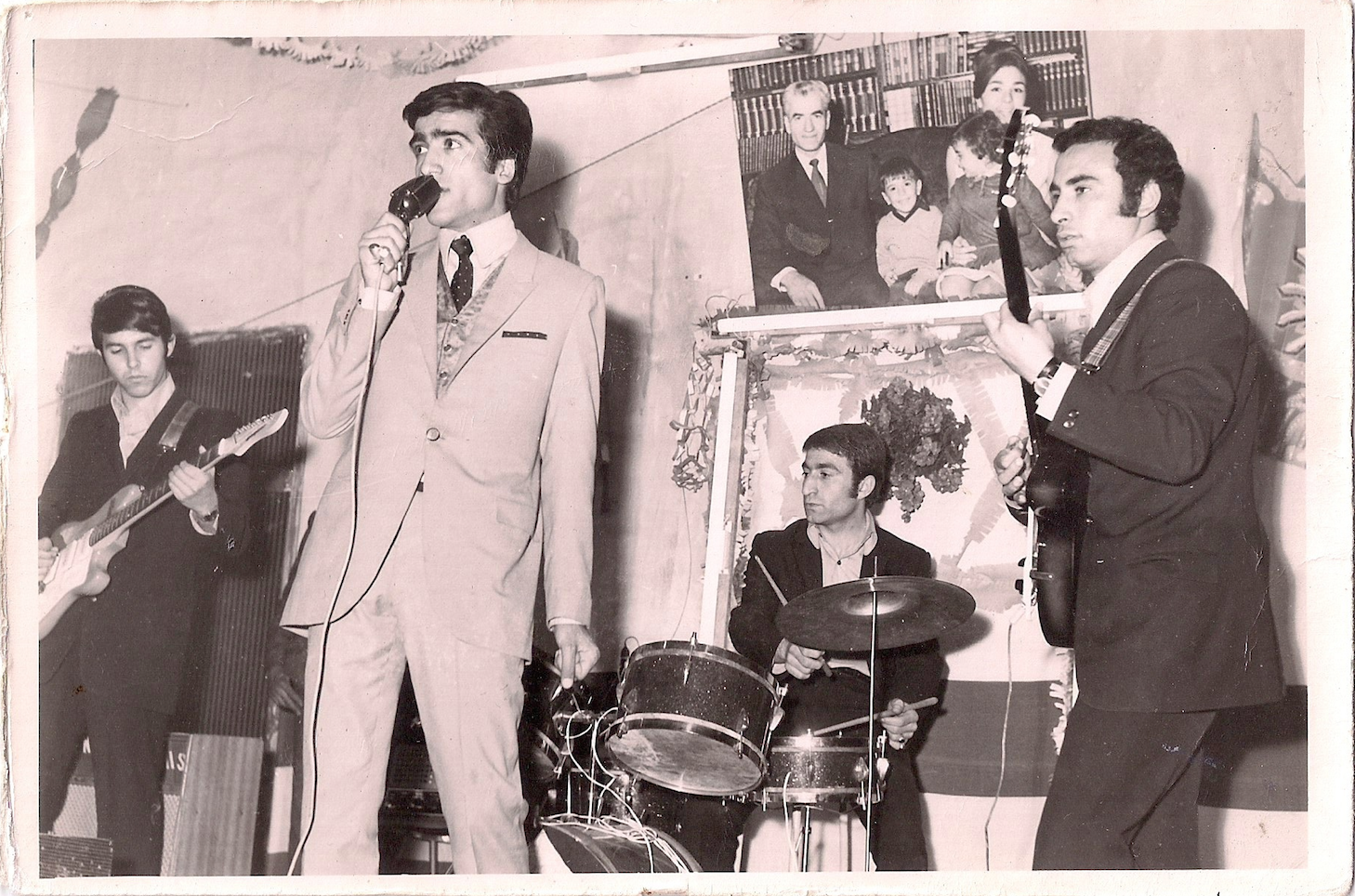 Joe's father (middle) playing his only rock show with his still best friend on guitar (right). Despite how it may look, the performance was apparently awful. In the background photo is the Shah with the royal family. 