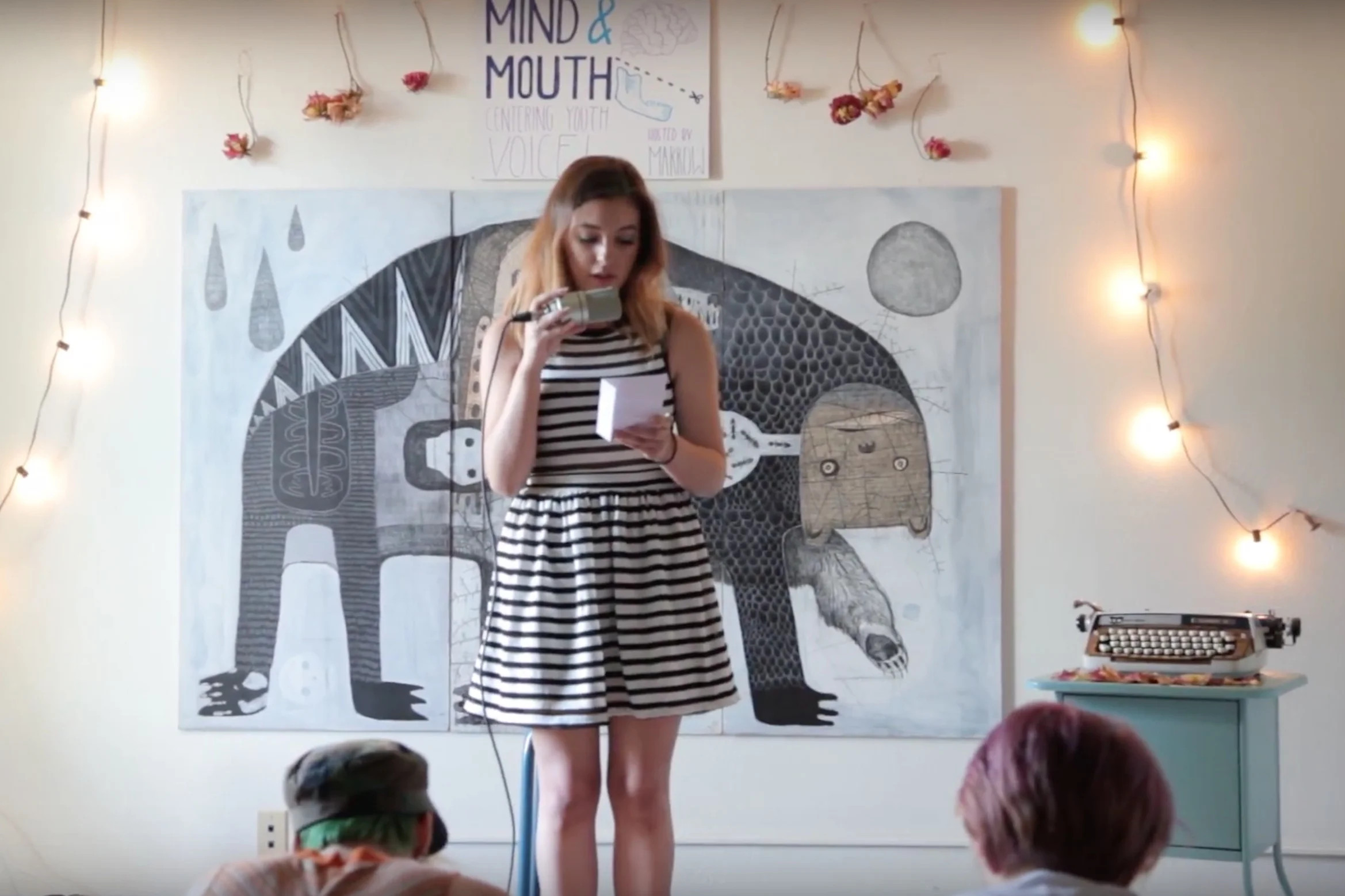 Kylin performs in front of one of Jesse's paintings at an open mic.