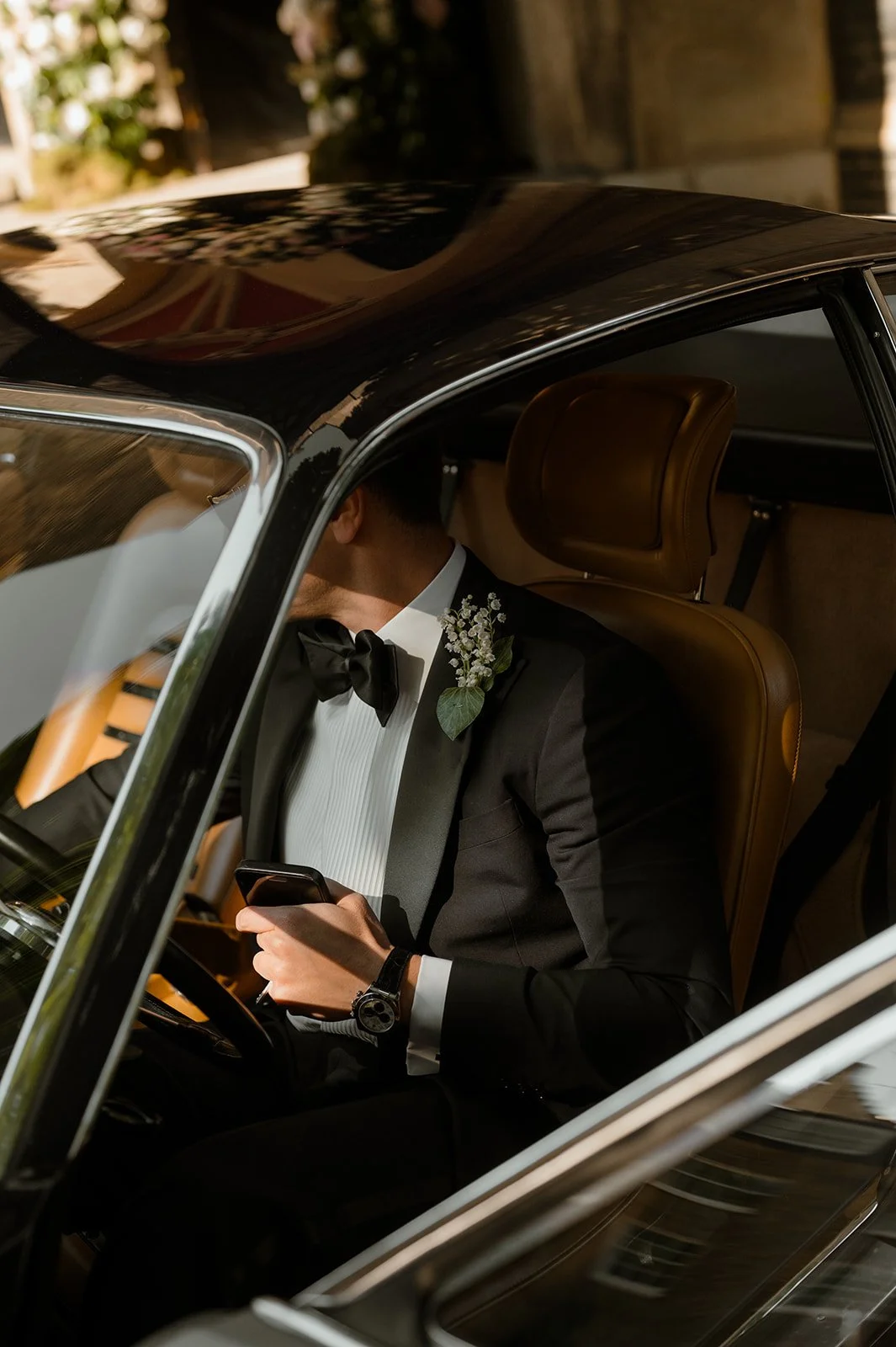 Groom sitting in the back of a car checking his phone before the wedding ceremony.