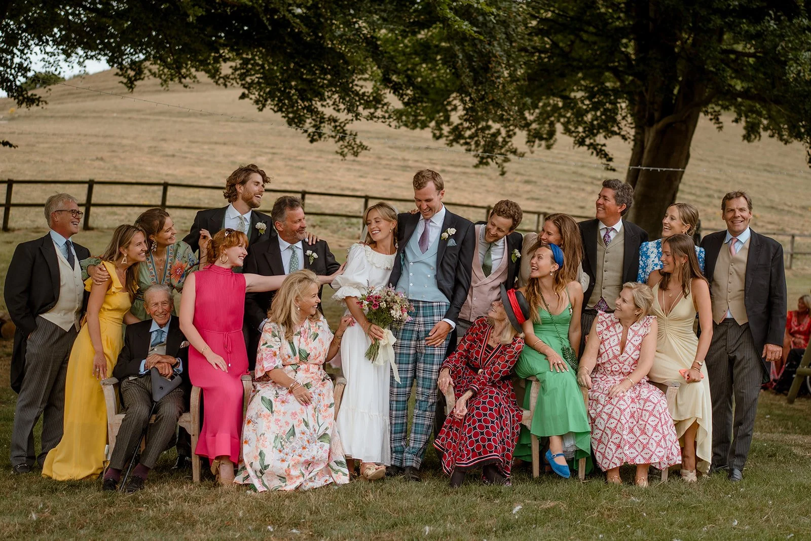 Bride and groom surrounded by smiling family and friends in a natural wedding group shot outdoors.