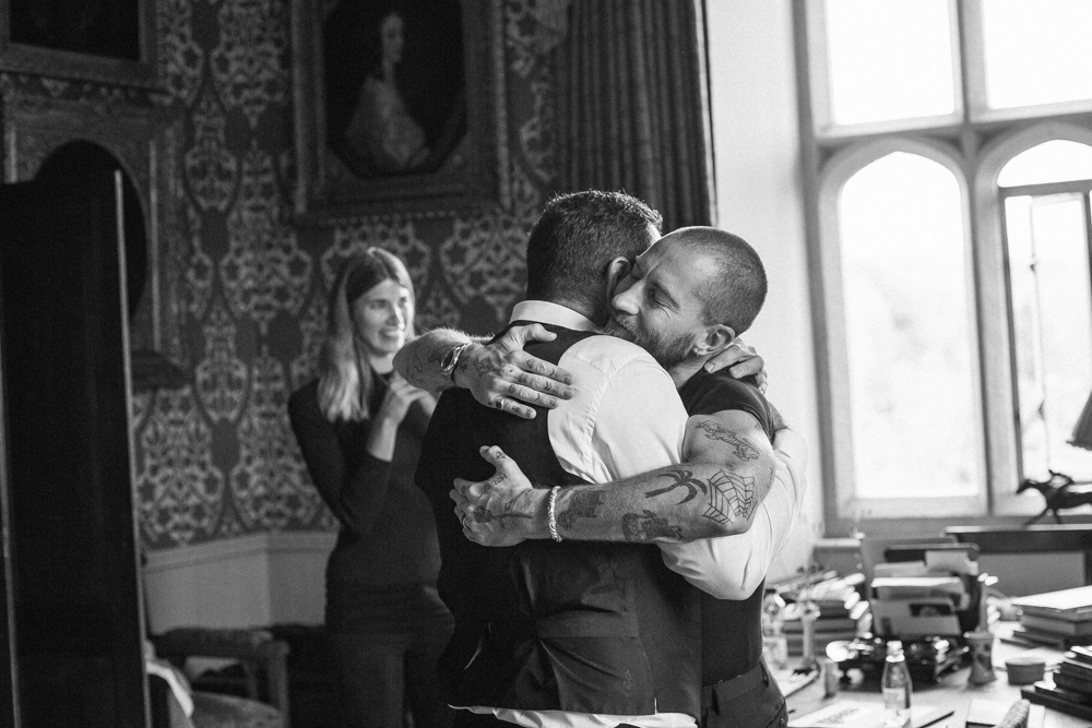 black and white two men embracing in light filled room at wedding