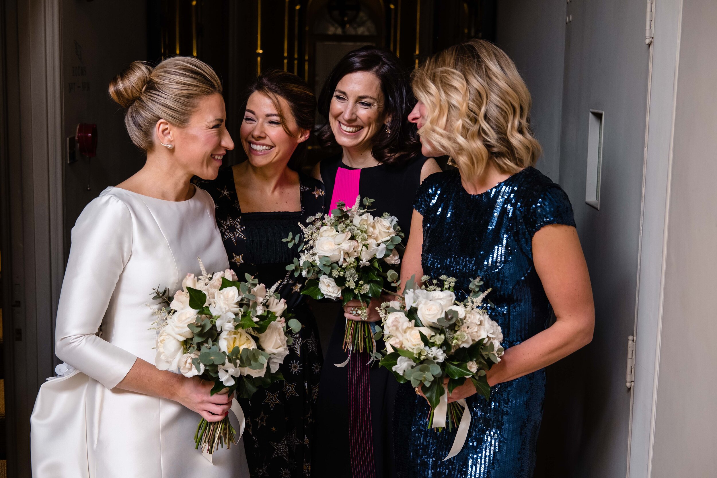 bride and bridesmaids stood with floral bouquets laughing together