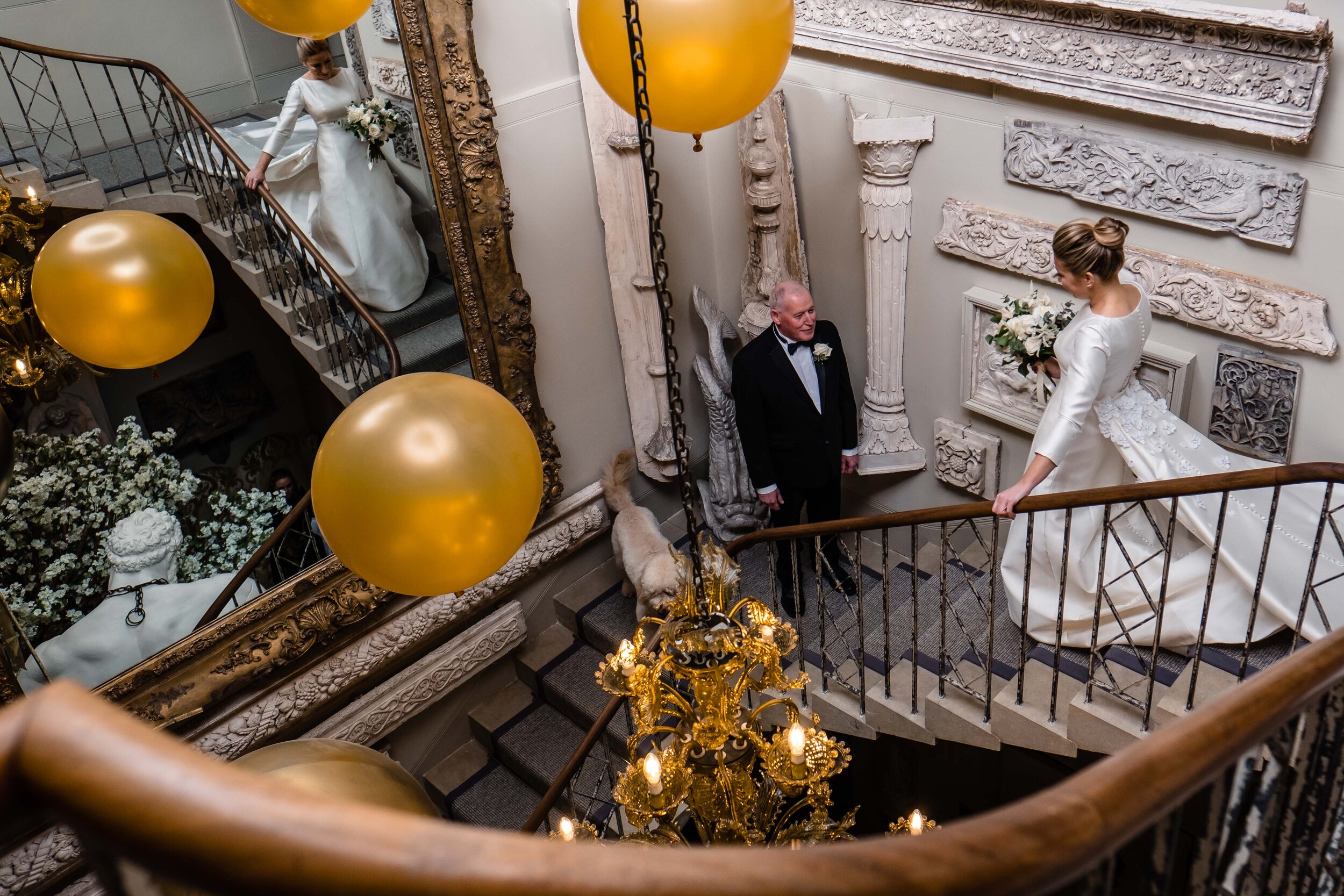 bride walking down grand staircase with yellow balloons to meet her father
