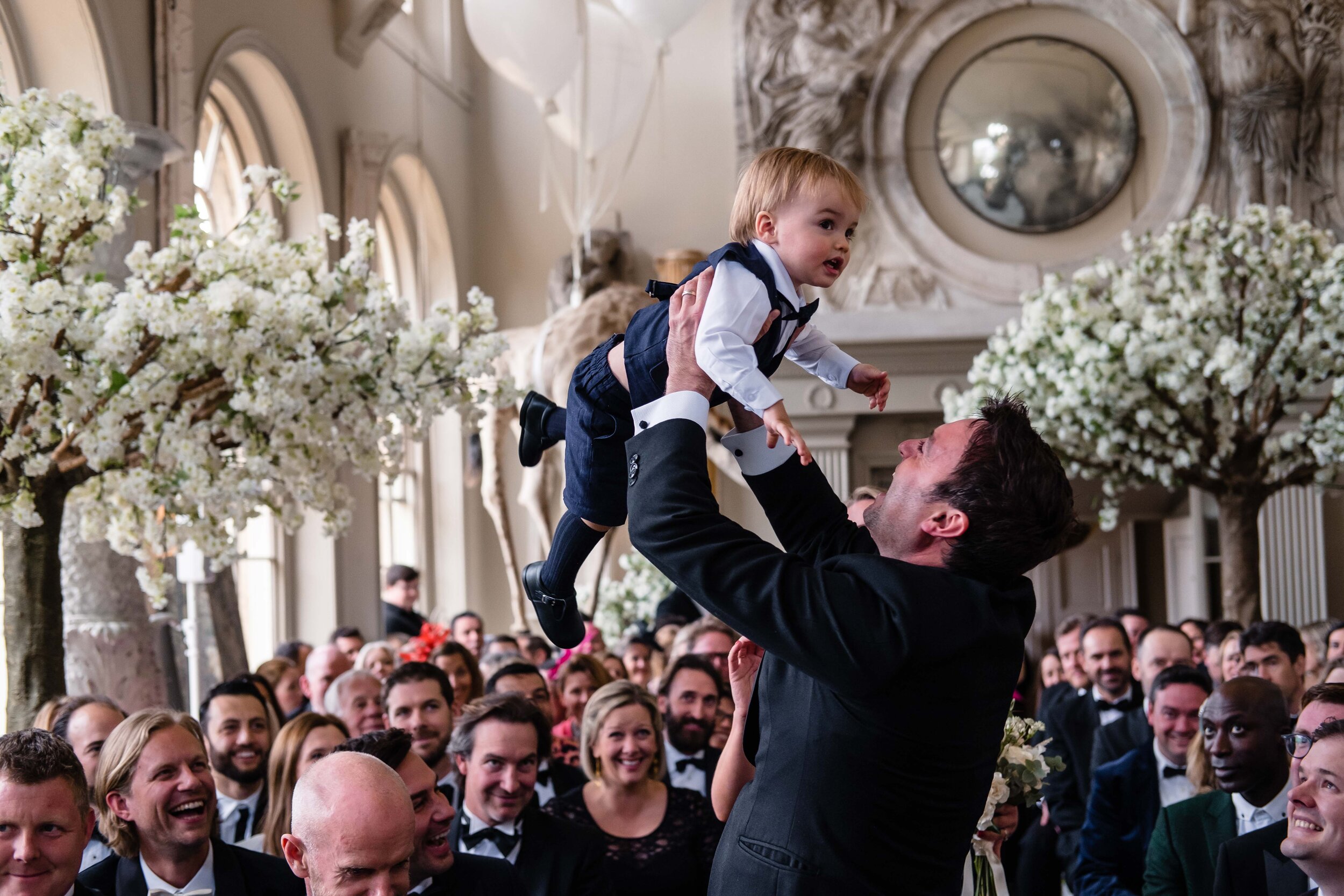 wedding guest throwing a little boy up into the air with white floral arrangements