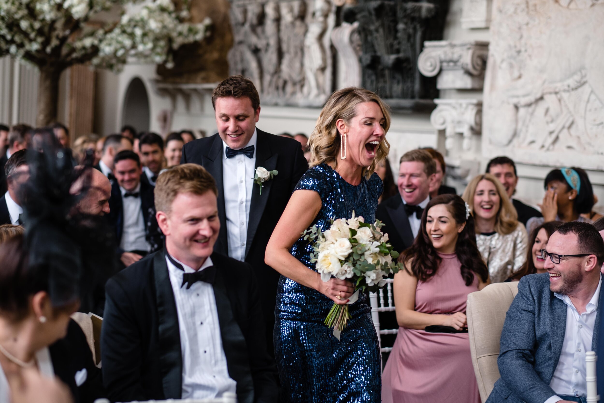 room full of wedding guests at Aynhoe Park with bridesmaid in blue dress laughing