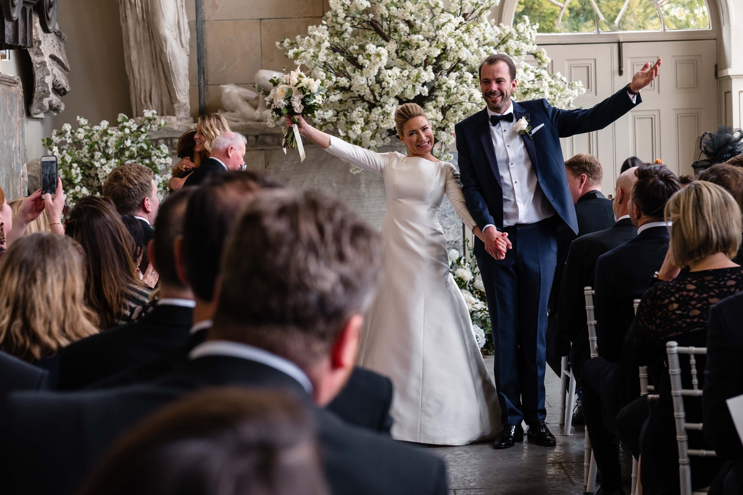 bride and groom at the end of the aisle with their arms raised in celebration