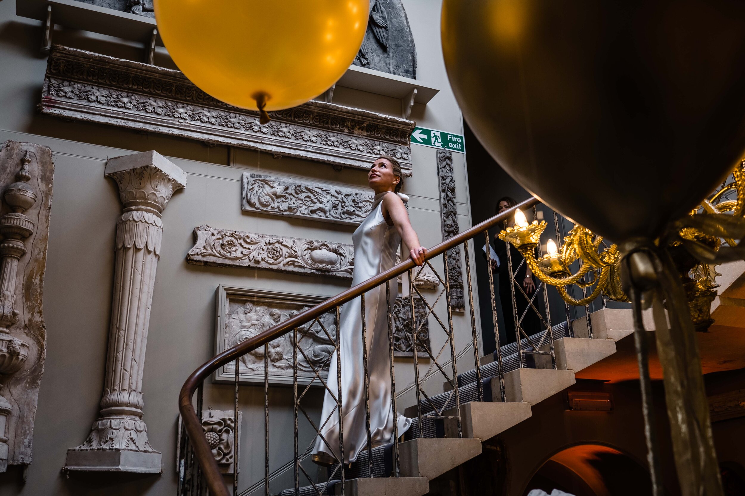 Aynhoe Park wedding photograph bride walking down the stairs with golden balloons