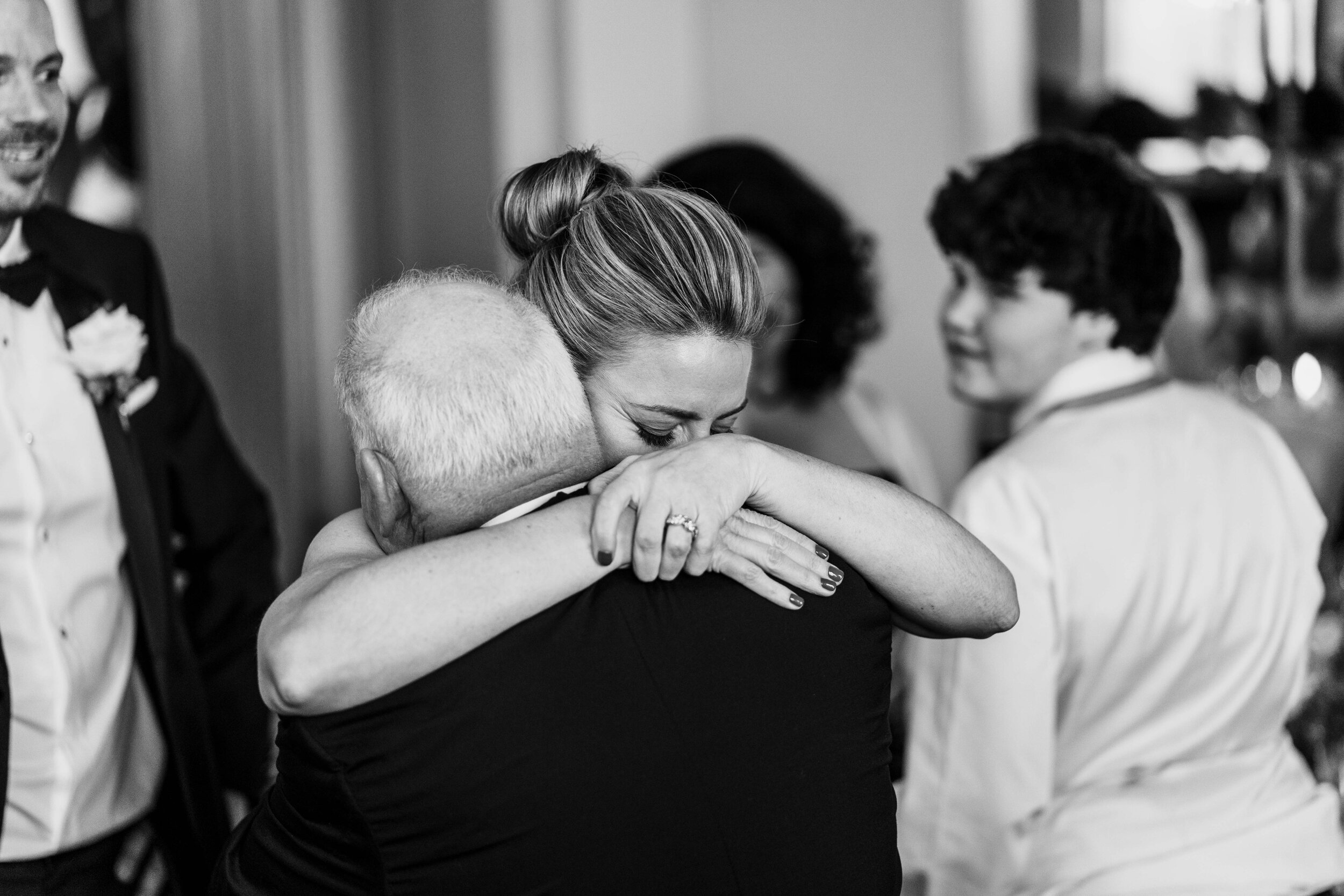 bride hugging father, faces obscured with another guest looking on