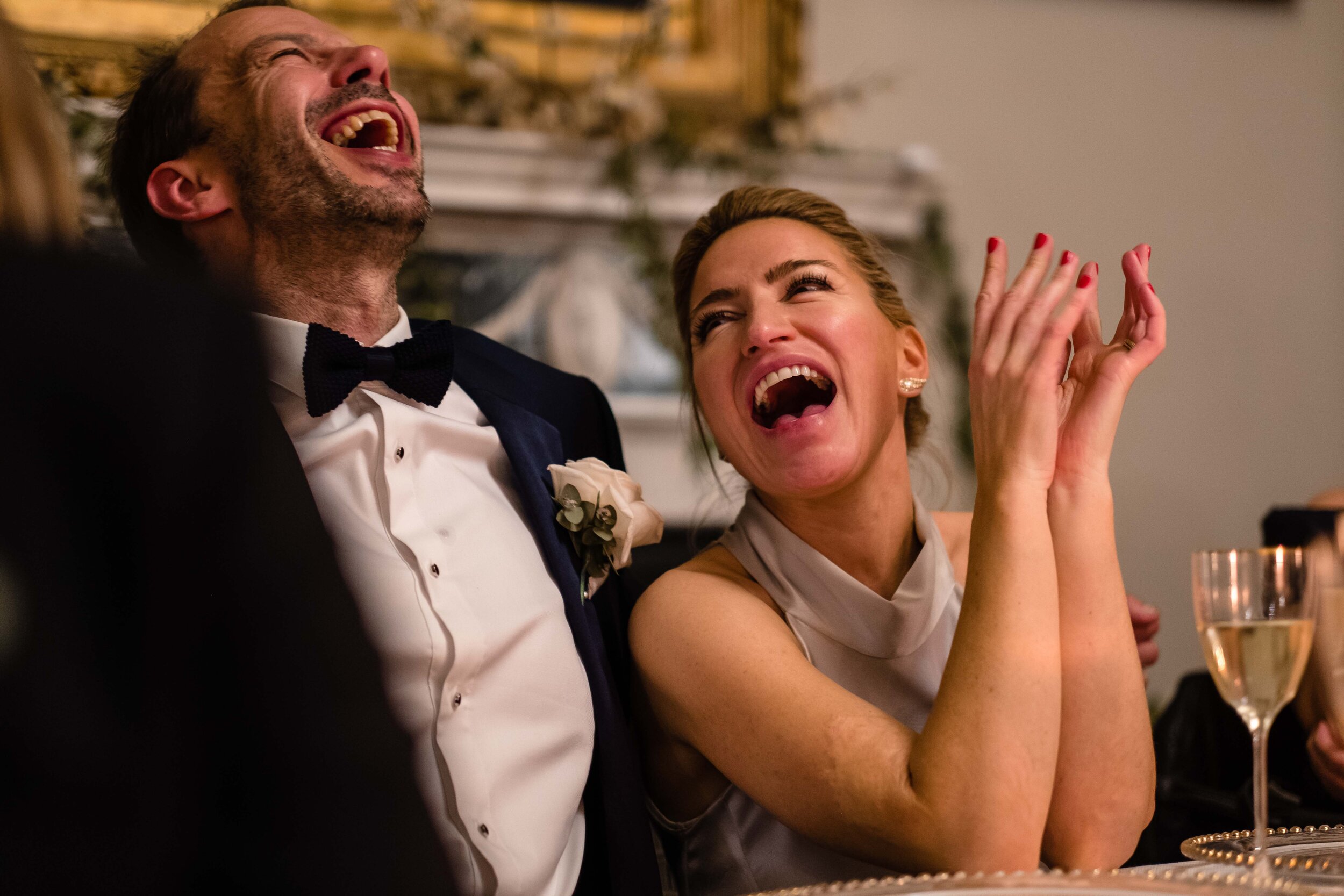 bride and groom laughing sat at table looking at each other