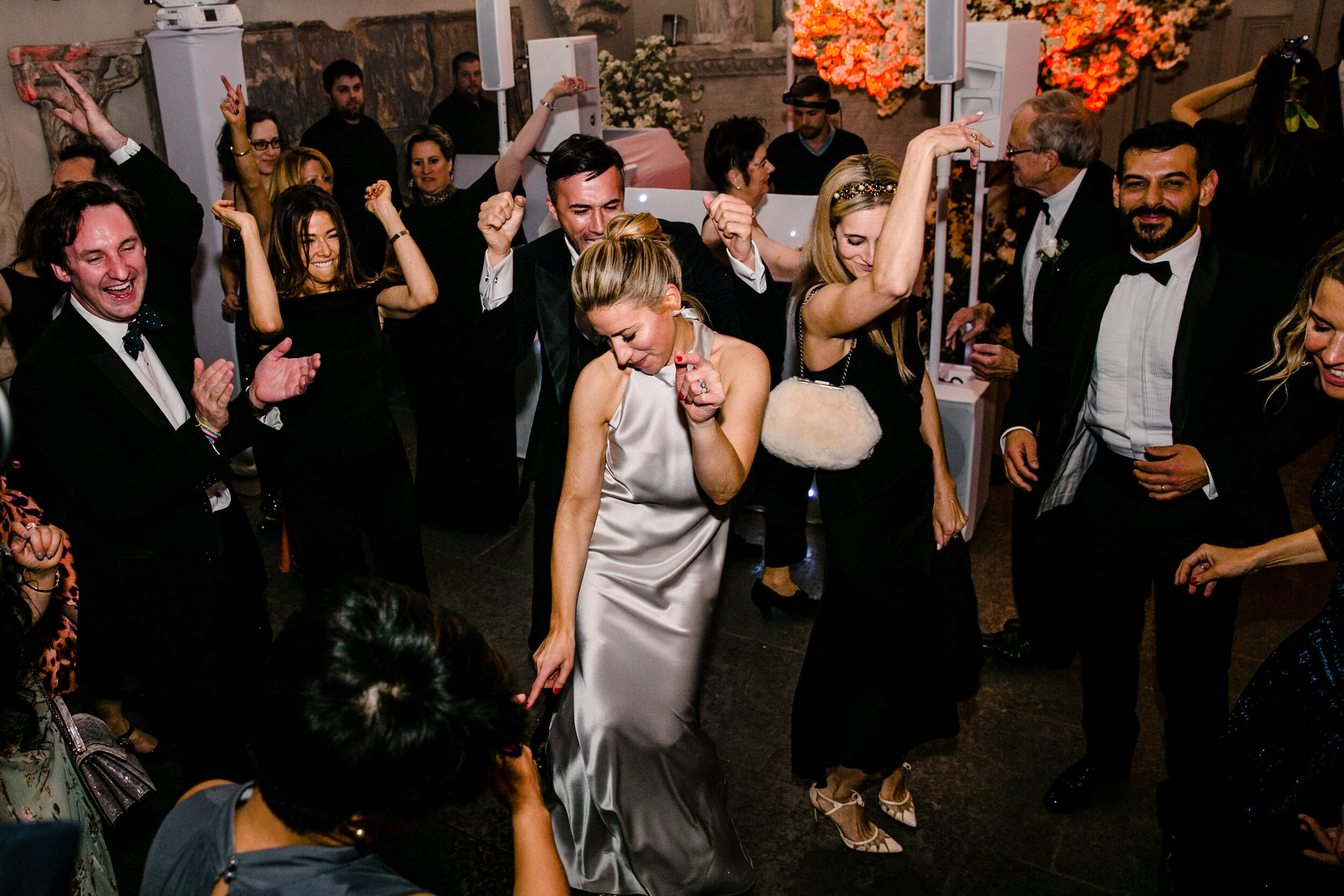 bride dancing in the middle of a group of people clapping wearing silver halterneck wedding dress