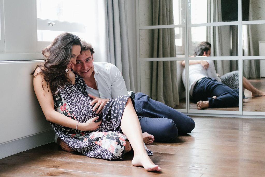 couple sitting on the floor below a window by a mirror divided into squares she is pregnant