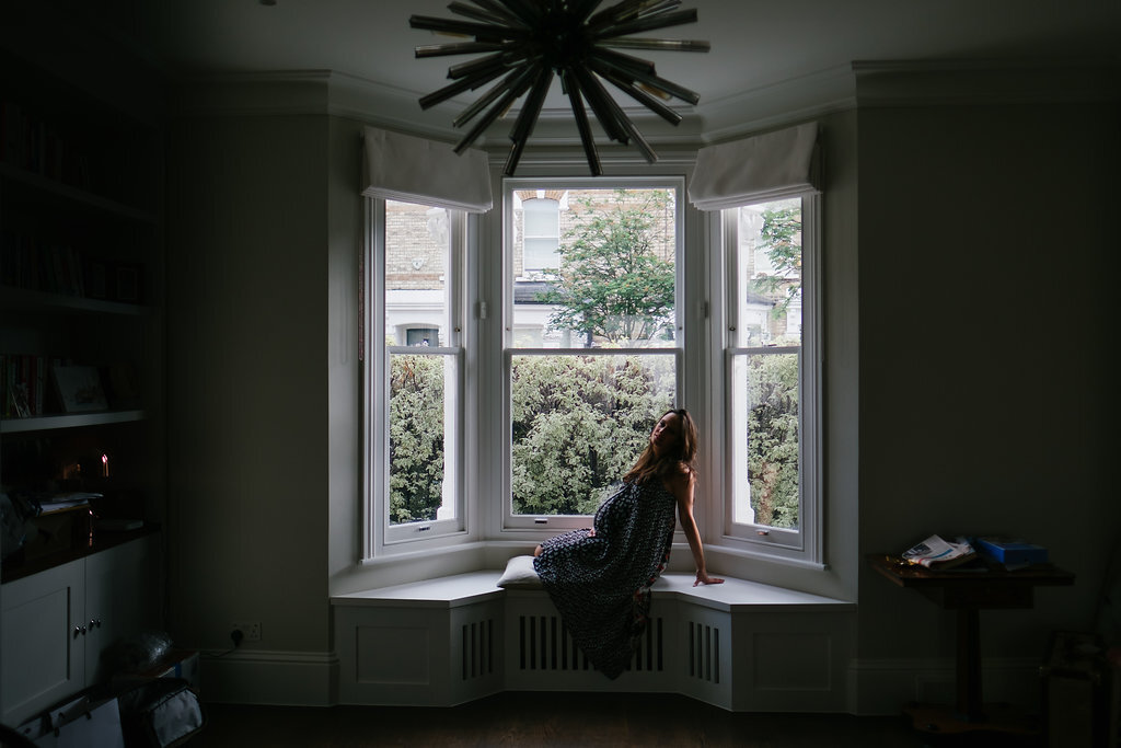 pregnant woman photographed sitting in front of large bay window in silhouette