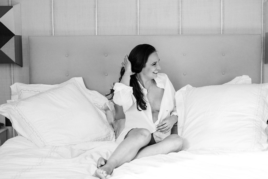 face on woman sitting on bed with legs stretched out in front in black and white holding her hair back