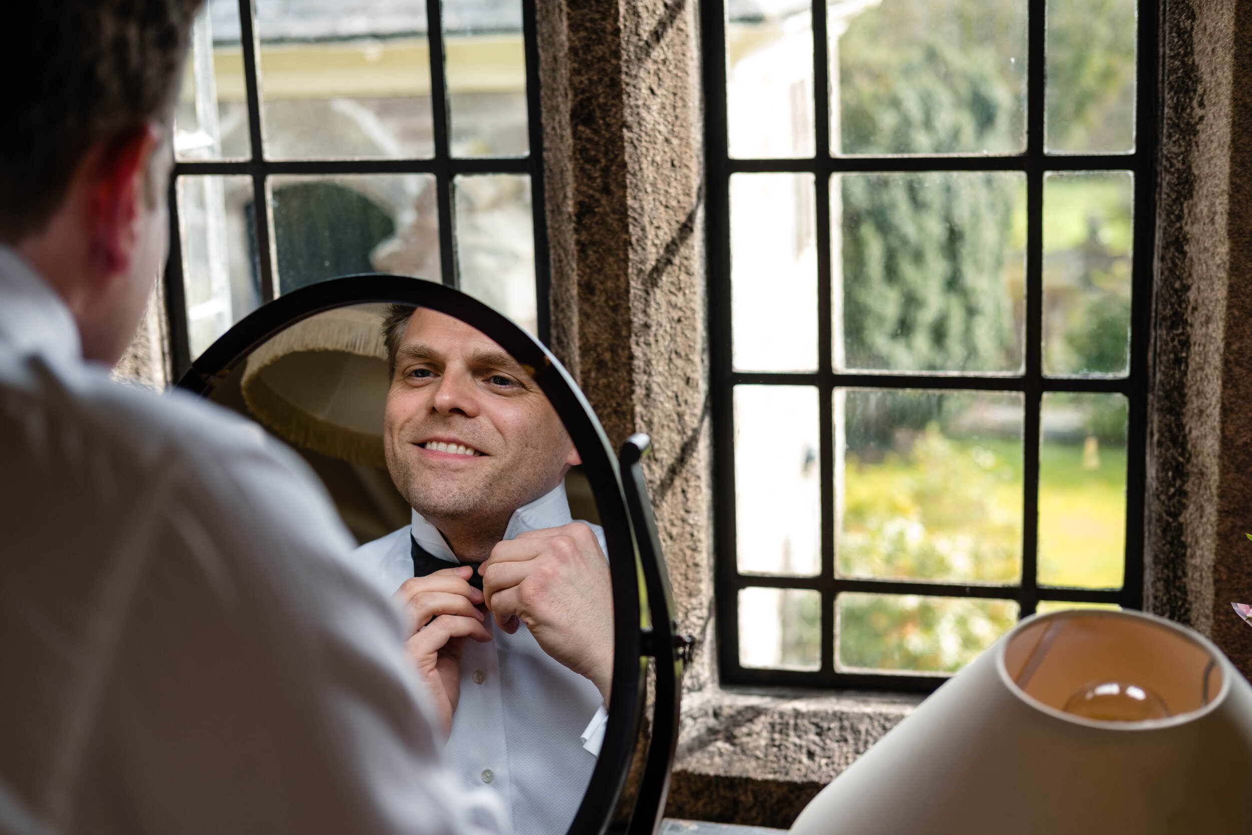 groom looking in mirror tying up bow tie