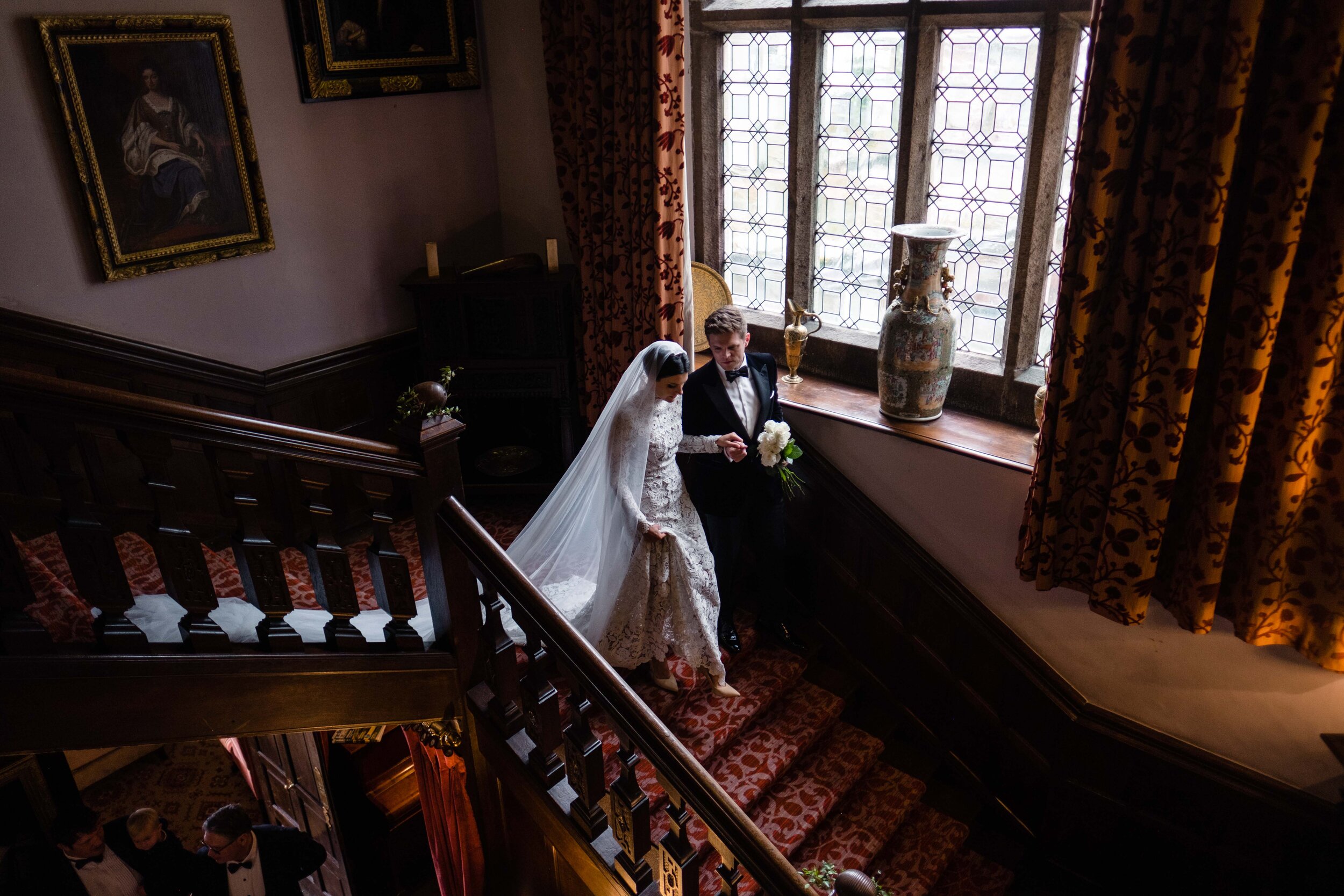 bride waking down grand staircase at Lewtrenchard Manor