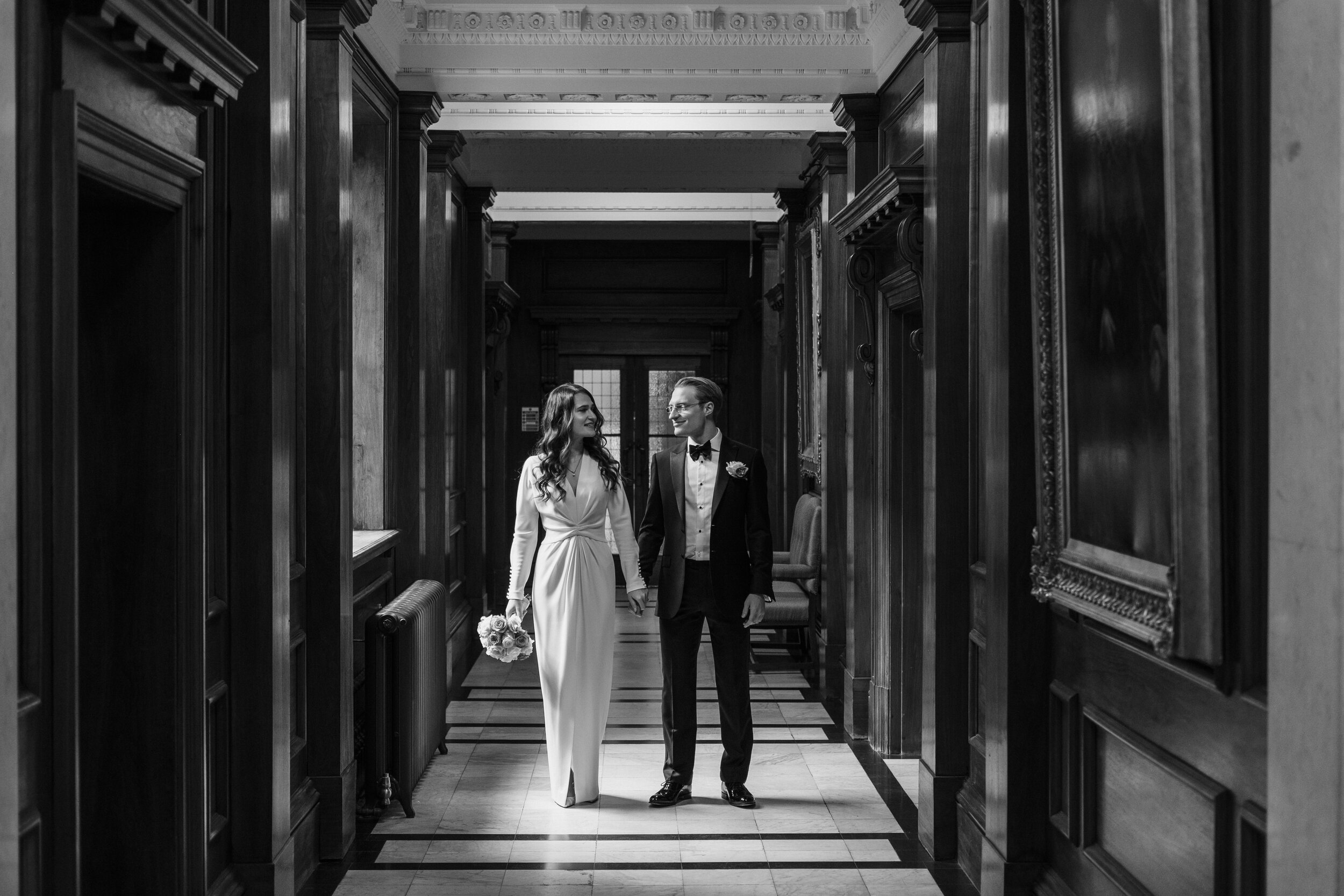 black and white bride and groom walking down sunlit hall 