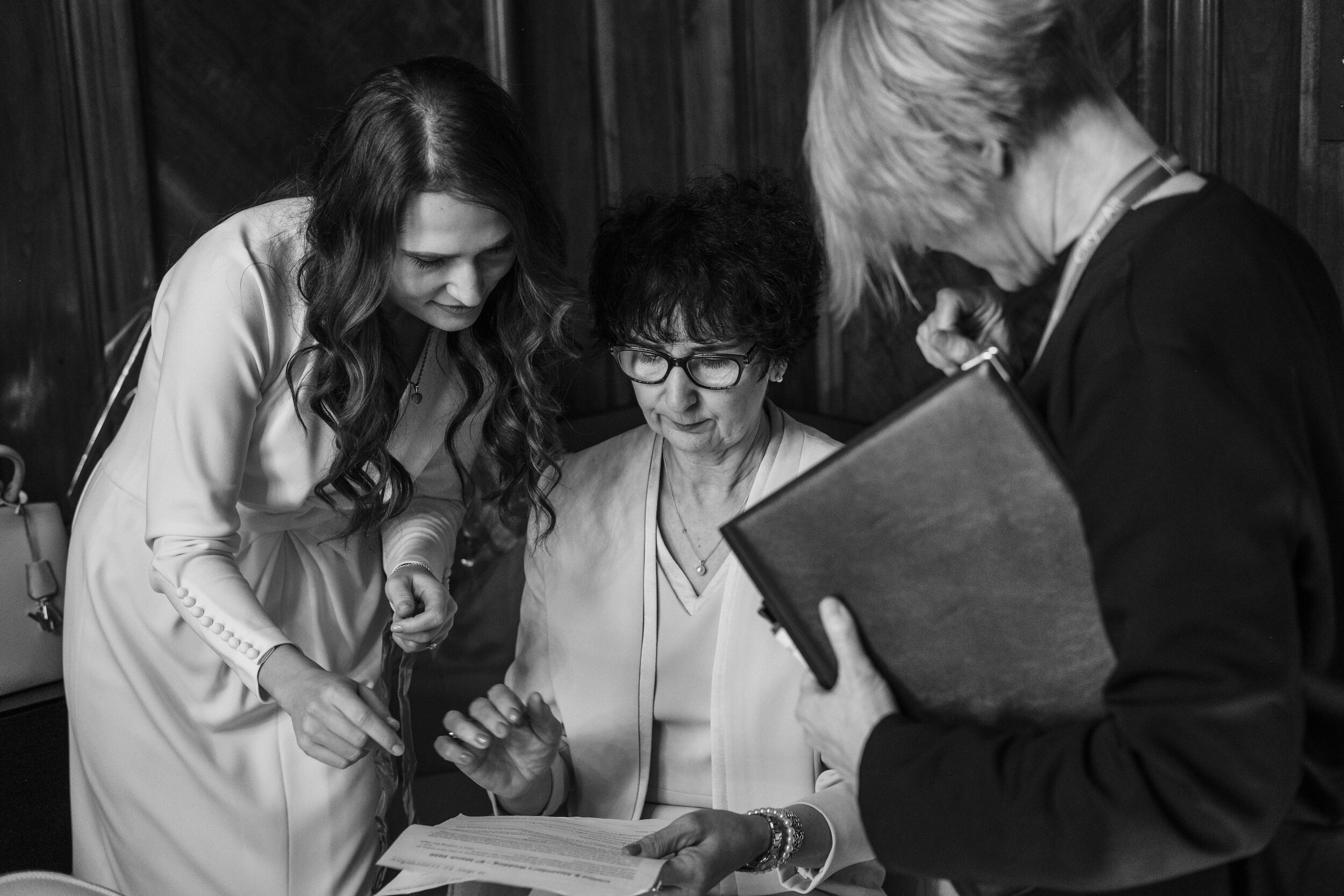 close up of woman signing marriage register surround by bride and registrar black and white