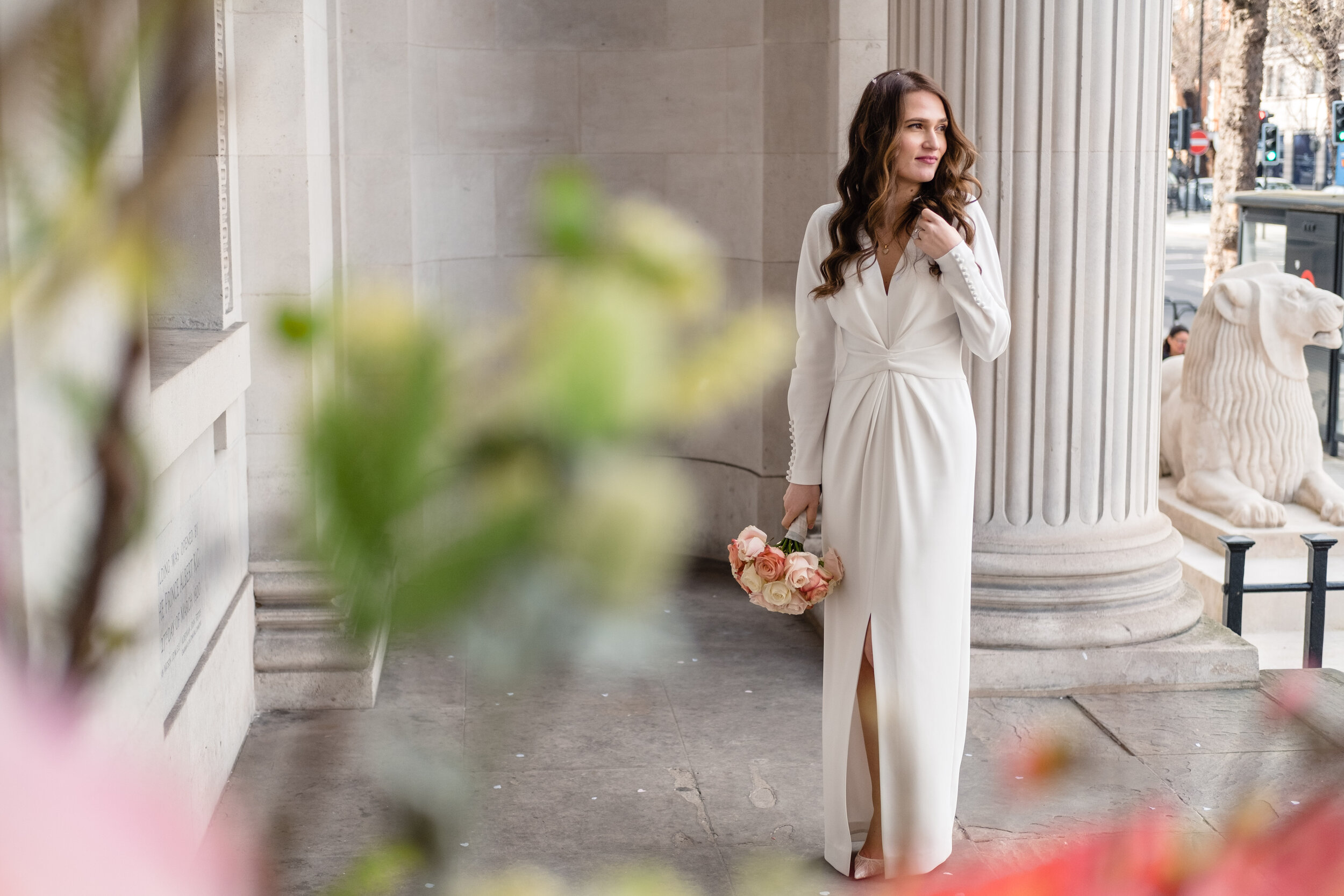 bride standing next to pillar with foliage in foreground