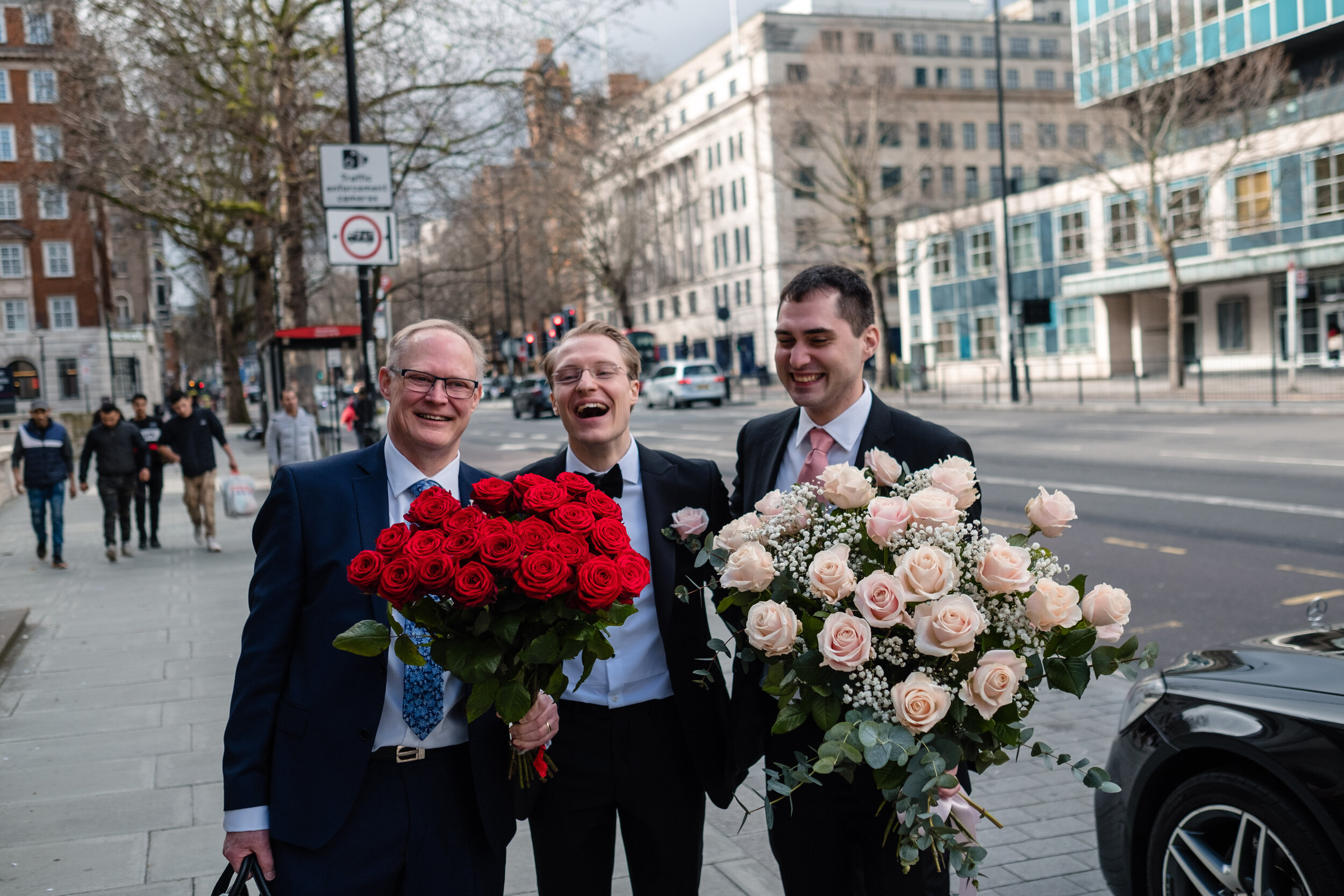 three male guests laughing and holding big bunches of roses