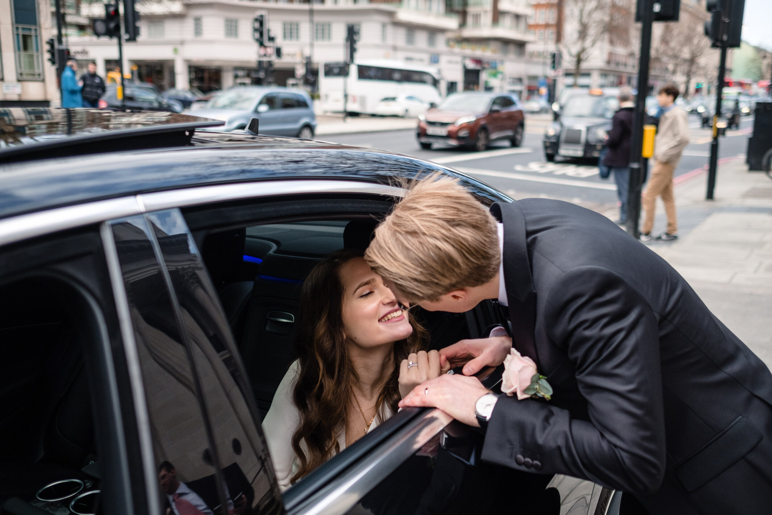 groom leaning into a car window to kiss a bride in the car