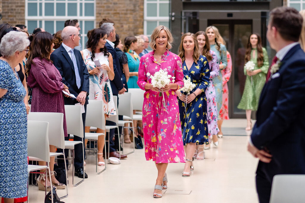 bridesmaids in pink floral dresses walking up the aisle at hackney town hall