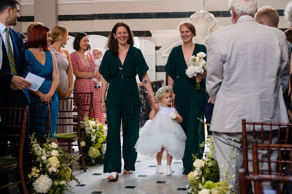 two adult bridesmaids and flower girl walking down the aisle