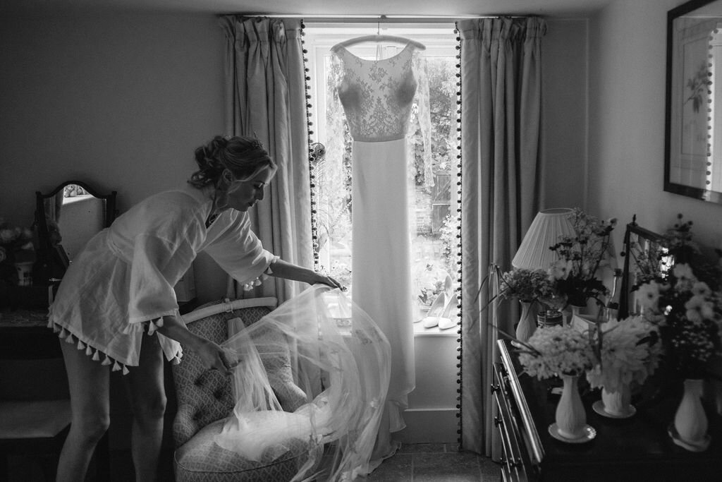 black and white bride adjusting wedding dress hanging in a window