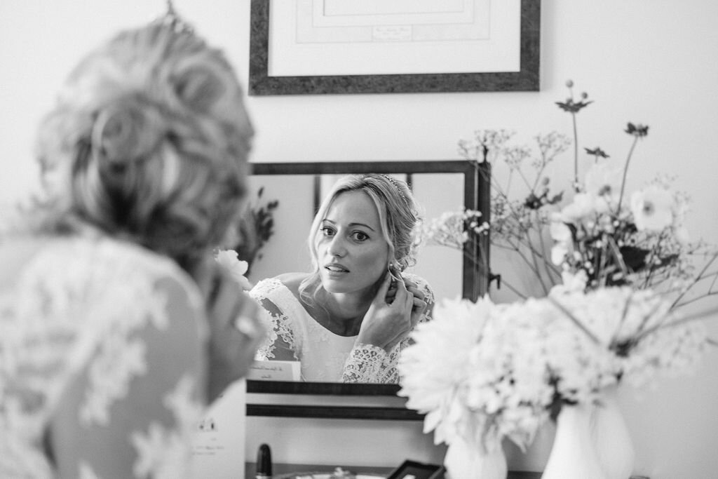black and white image of bride looking in mirror and fastening earring