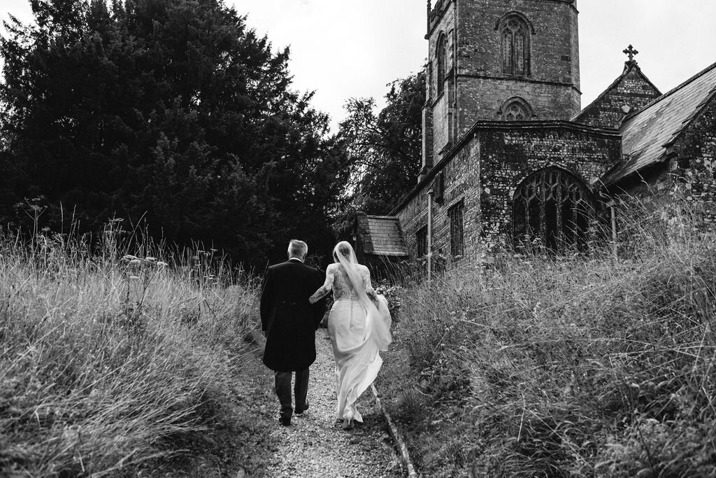 rear view black and white of bride and father walking up path to church