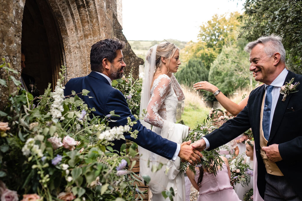 two men shaking hands outside church by bride