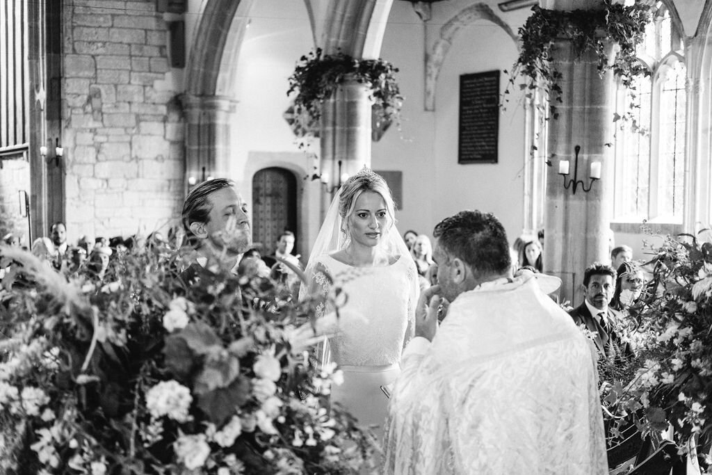 black and white of bride and groom standing in church in front of vicar