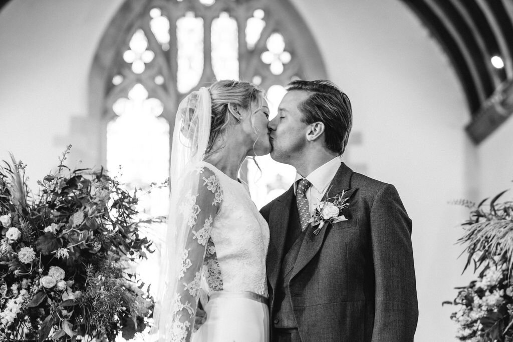 black and white bride and groom close up from below kissing in front of stained glass window