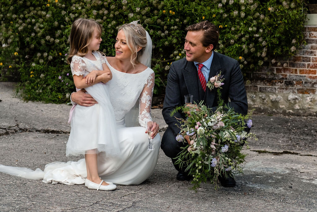 bride and groom crouched down with flower girl groom holding bouquet