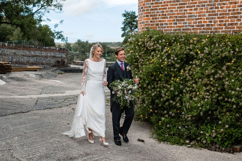 bride and groom walking in front of hedge and red wall