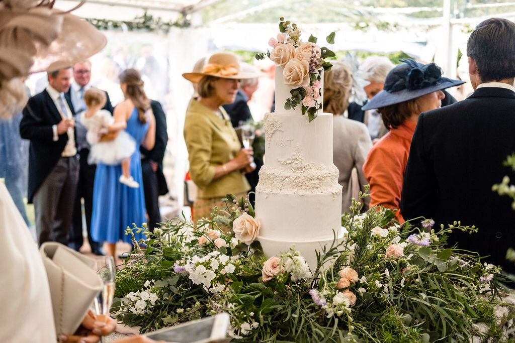 large wedding cake surrounded by greenery and guests