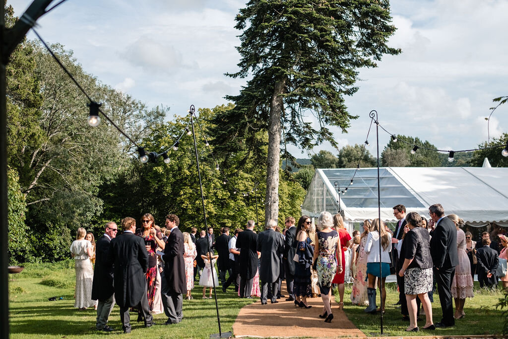 guests standing on lawn outside marquee wide shot with trees